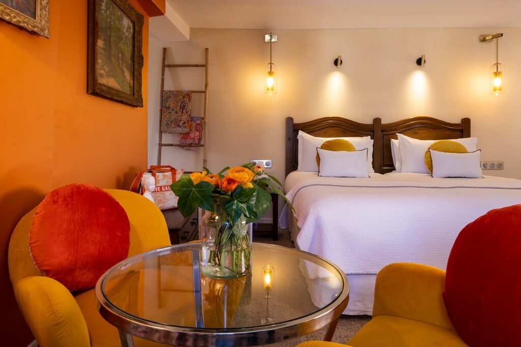 room with king size bed, orange fabric and sitting area with armchairs and table - boutique hotel Paris - hotel des marronniers