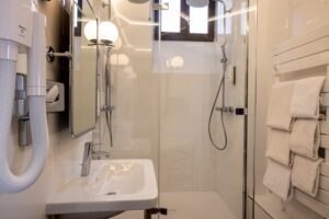 white bathroom with two showers, window, sink and hair dryer - large room in Paris - hotel in Paris