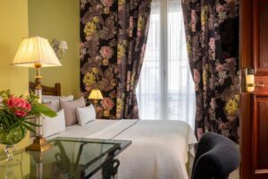 photo chambre hôtel de charme lit double avec tissus vert et rideaux fleuris