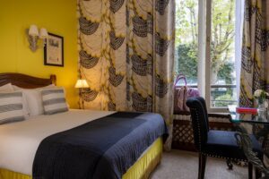 hotel in Paris - room with bed, pillows, yellow fabrics, window over the garden - desk and black chair - romantic room Paris