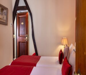 photo chambre hôtel de charme deux lits blancs avec couvre lits et coussins roses, poutres apparentes