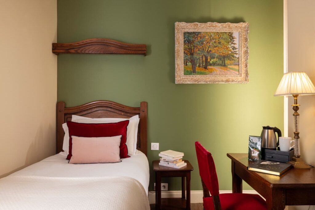 chambre solo hôtel de charme paris : lit individuel, coussins roses, tissu vert, bureau en bois et chaise rouge