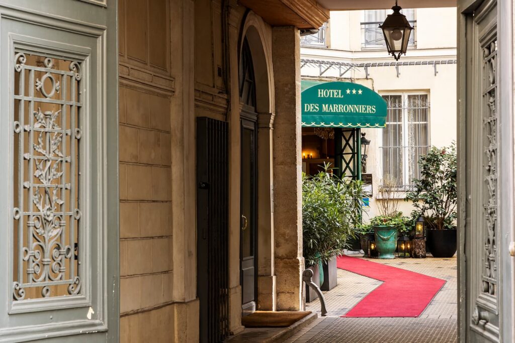 entrance of the hotel des marronniers, in a courtyard, with read carpet and hausmanian building