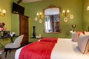 two beds, pink pillows, green fabric, large mirror, grey chair, desk, courtesy tray and decoration - large room in Paris - hotel in Paris