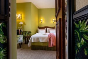 photo chambre hôtel de charme porte ouverte sur chambre verte avec lit blanc et veste rose