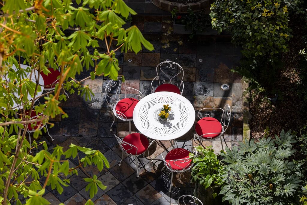 vue sur le jardin avec table, chaises blanches et coussins rouges, feuilles des marronniers - hotel de charme paris