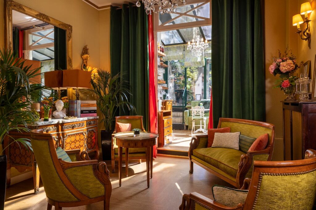 réception hotel trois étoiles avec canapé et fauteuils verts, rideaux menant à la véranda et au jardin 